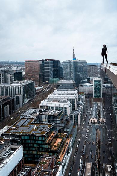 silhouette of a girl standing on the edge of a tall building with the city below and reflects in the glass windows