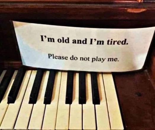 A piano with a notice upon t stating"I'm old and tired. Please do not play me"