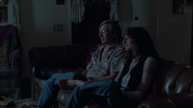 Screenshot of the movie Repo Man. It's Otto's hippie parents mesmerized by the Reverend Larry show on TV and telling him they've given away all their money to send "bibles" to El Salvador.