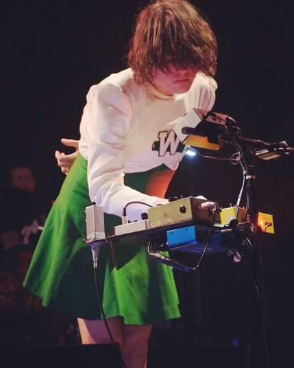 A photo of My Chemical Romance lead singer Gerard Way, leaning over a soundboard and wearing a green and white cheerleader's uniform.