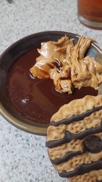 A small bowl with chocolate syrup, peanut butter, and a fudge stripe cookie about to get dunked in it
