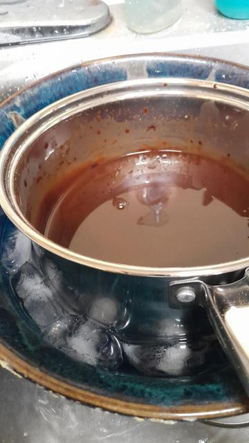 Chocolate syrup in a pan placed in a bowl with water and ice to cool down