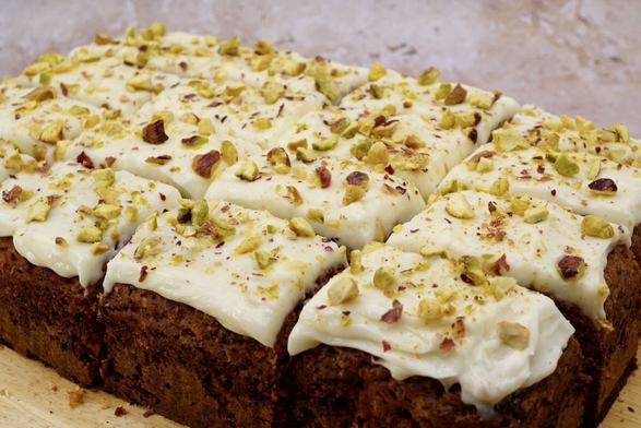 A rectangular carrot cake with cream cheese frosting and  chopped nuts cut into portions.