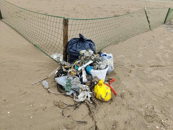 Eine größere Menge Strandmüll, aufgetürmt zu einem Haufen an einem Sandstrand. 