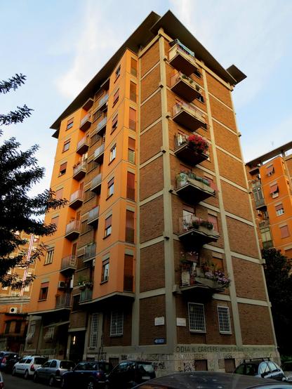 Picture of a tall, eight-story residential building constructed of concrete and brick. The street-facing façade is dominated by a protruding volume that houses bay windows and balconies.