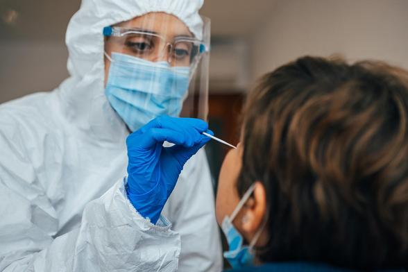 Nahaufnahme einer weiblichen medizinischen Fachkraft in PSA, die einer Patientin einen Nasenabstrich einführt. 