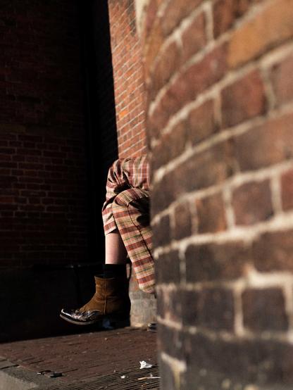 Feet behind a wall, the pants match the brick wall
