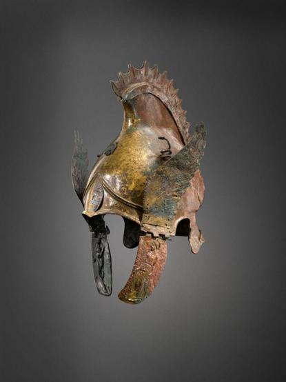 Casco alado, con dos pequeñas serpientes enroscadas detrás. Tiene una cresta similar a una aleta de pez. En la solapas sobre las mejillas tiene relieves de Niké y Artemisa.