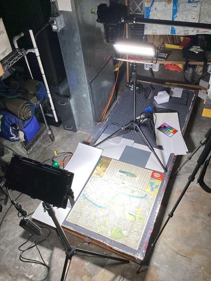 A document scanning setup in a basement — two studio lights illuminate a map on a low platform, with a camera on a boom overhead