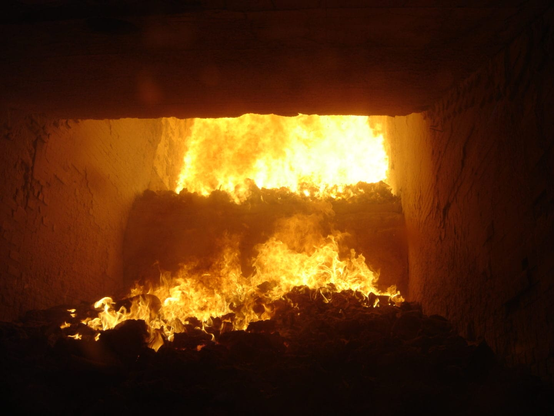 The inside of a lit industrial furnace. Not a lot is visible but for flames, solid walls, and the silhouettes of whatever's burning.