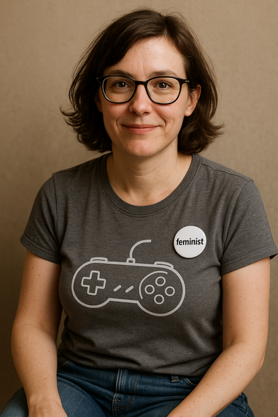 Ca. 40 jährige Frau mit halblangen Haaren (Chat GPT sagt "Messy"), Brille mit schwarzem Rahmen, schmuckloser "feminist" Button, graues shirt mit einem Gaming Controller
