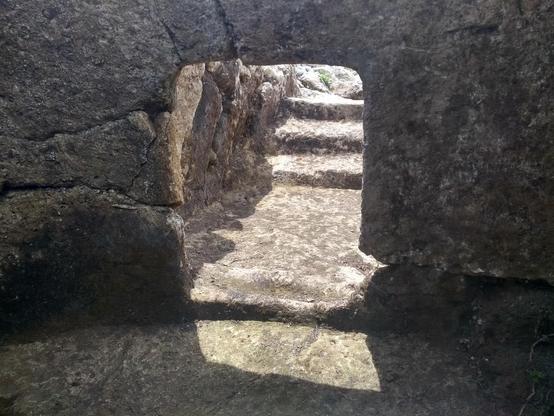 Stoned carved steps leading down into partially underground chamber tombs. The daylight catches the steps and entrance.