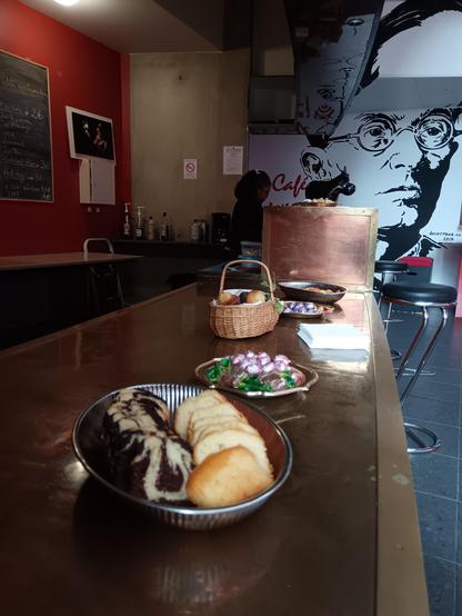 Une photo du goûter sur le thème de Pâques. Des oeufs en chocolat sont disposés dans des récipients, du quatre-quart et du marbré découpés sont au premier plan dans un plat. On aperçoit plus loin un panier en osier rempli de madeleines. Tous ces récipients sont posés sur un bar. 