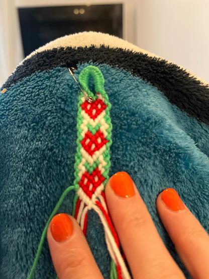 Ein geknüpftes Bändchen, auf dem Erdbeeren auf weißem Hintergrund und grüner Umrandung sind.