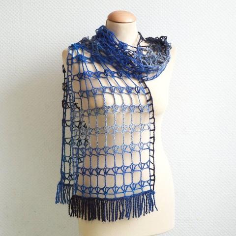 An airy crochet scarf in a blue gradient yarn, is shown draped on a mannequin against a white background.