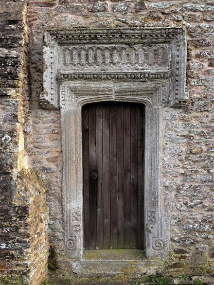 A dark wood door with a carved stone surround. Above is more highly carved stone with characteristics of both Tudor and Jacobean work.