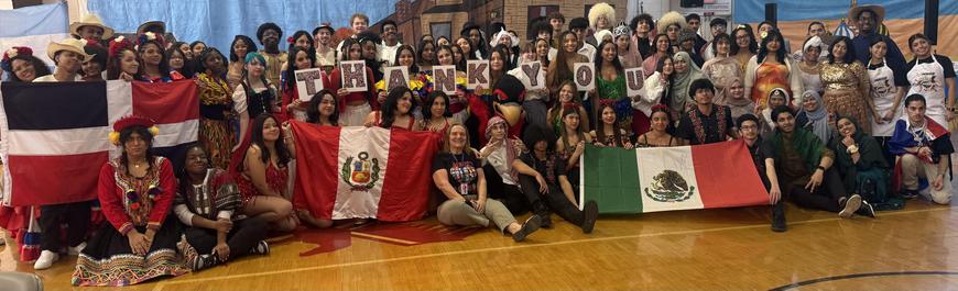 Large group of US HS students, repping their home countries at an International air their HS holds each year.  Many students are in traditional dress.  Students are holding the flags of Mexico, Peru and the Dominican Republic can be seen in front