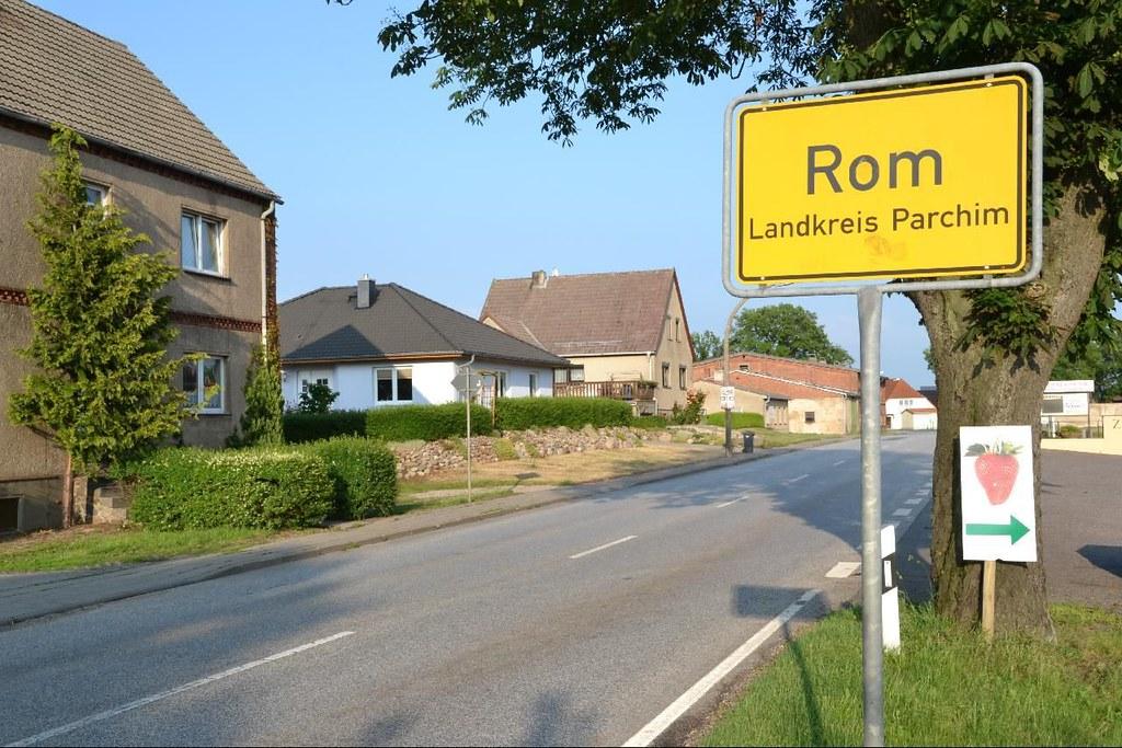 Das Foto zeigt eine Ortseinfahrt mit ländlicher Bebauung. Rechts ein gelbes Ortsschild mit der Aufschrift
Rom
Landkreis Parchim
