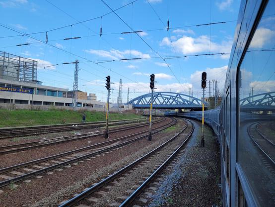 Train turning left under a bridge next to 4 tracks.
