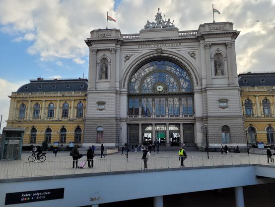 Keleti station building seen from outside. Magestic old building, with white/grey stones in the middle part, and yellow for the sides. An opening leads to the underground & metro network.