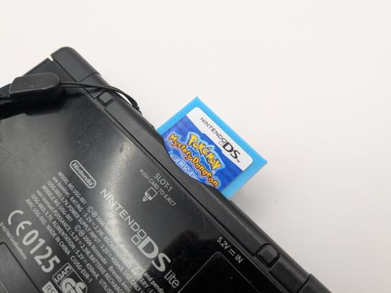 A ds lite closed laying face down with a cart ejected from the cart port. The cart is blue with a pokemon mystery dungeon lable