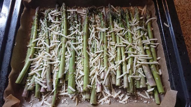 gruner Spargel auf einem Backblech mit Salz, Pfeffer, Olivenöl und veganem Streukäse fertig für den Ofen