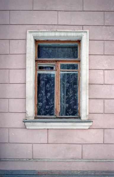 Old window with tulle against pink wall of old house.