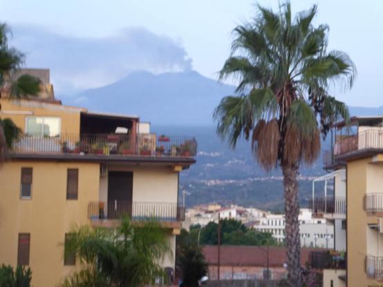 View through apartment blocks to Mt Etna with plume of smoke arising from its summit
