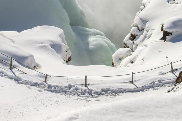A snowy landscape, a fence with footsteps next to it, some rocks. And light green-blueish white ice, with some mist of the waterfall, which is not visible in the photo. So mostly white. 