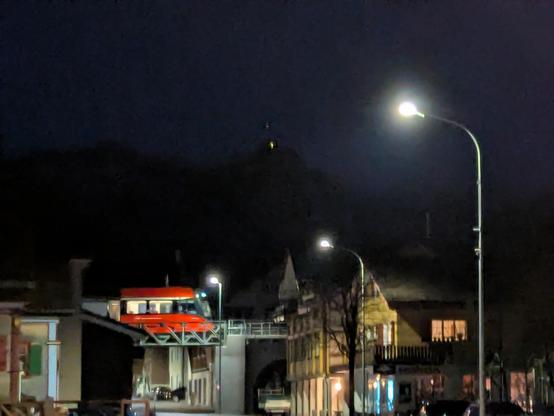 Un train rouge des Appenzeller Bahnen traverse un pont dans la nuit, le rouge se distingue du reste. Maisons typiques autour.