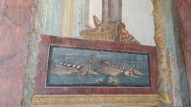 Photo of a detail of a fresco at Pompeii with two Roman or Greek galleys side by side with oars on both and warriors with shields and spears on board.