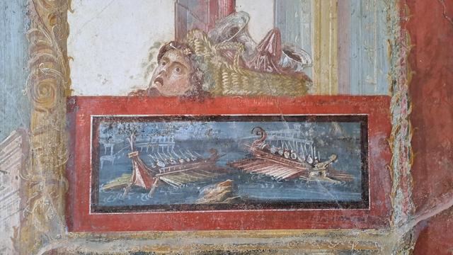 Photo of a detail of a fresco at Pompeii with two Roman or Greek galleys passing each other in the sea in perspective.