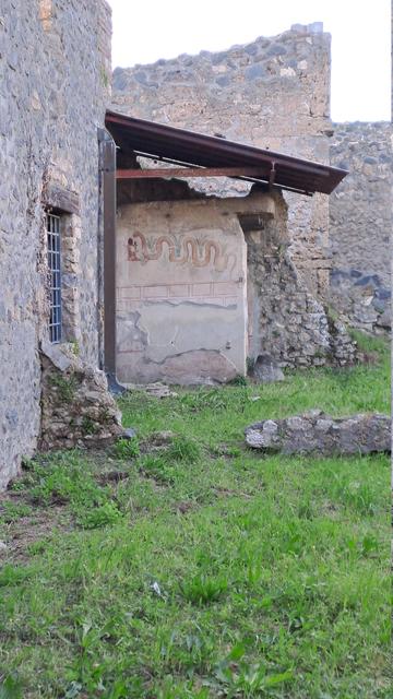 Photo of a Pompeii ruined house with a wall painting at the back which features a large snake curling across the scene with the head on stage right and overall very reminiscent of Egyptian and some early native American wall art