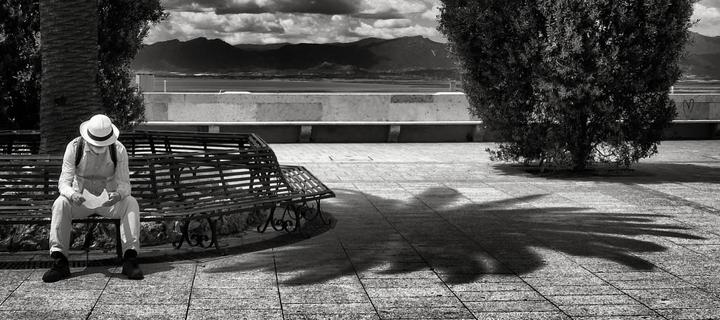 the reminder: a black-and-white photograph of a man sitting on a bench and reading a letter