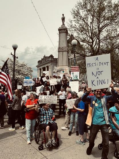 Protesters; includes an American flag, a man in in a wheelchair holding a "No Tyrants, No Despots, No Kings" poster and another sign reads: A President os not a king!