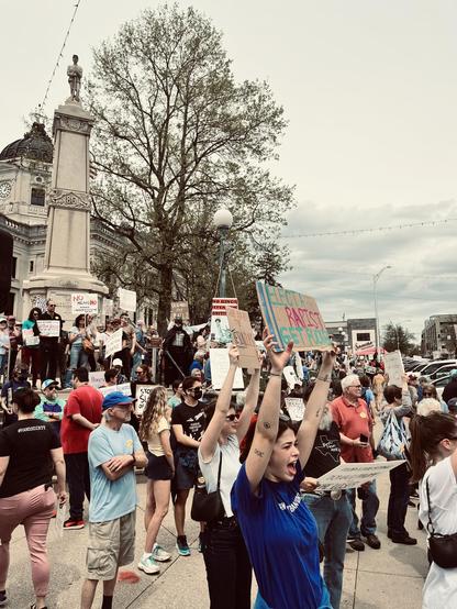 protesters in front of a midwest courthouse includes a young person shouting and holding up a sign that says, "Elect a rapist, get a fucker."