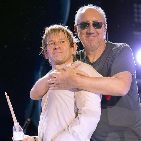 Zak Starkey being embraced at the shoulders by Pete Townshend wearing dark sunglasses. 