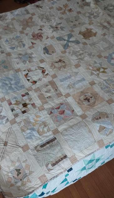a quilt it is different geometric designs in boxes in rows, lots of browns and tans and greys and white, swirly abstract floral type stitching over it 