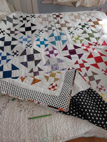 64.5 x 72.5 in (164 x 184 cm)quilt, a design of squares with triangles at each corner, each a different color, against a white background, the corner is turned up, showing the dark blue and white polka dot backing 