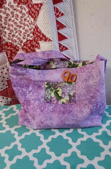 the reverse side of the bag, there is a small pocket on the lavender, the pocket is made of the same fabric as the arcs on the reverse side, the orange handles of scissors sticking out of it 