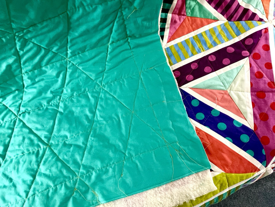 The back of the quilt. It is a teal/aquamarine color. You can see the quilting shape stitched on it