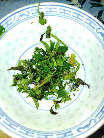 A small bowl containing chopped lemongrass, basils, oregano, sage and rosemary.