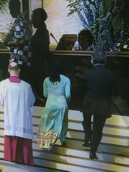 Uma senhora nas celebrações pascais do Vaticano com um vestido com uma foto da basílica da São Pedro impressa no dito.