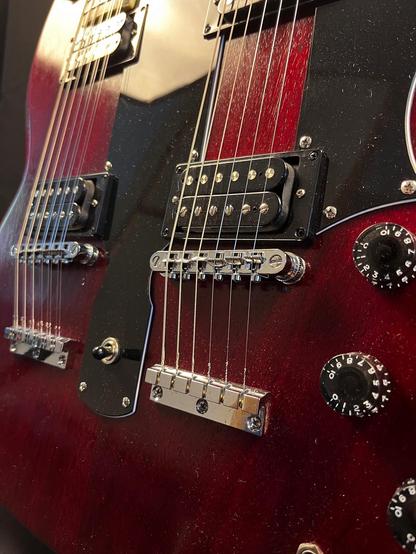 Nahaufnahme einer rot-schwarzen Doppelhals E-Gitarre mit Tonabnehmern, Saiten, Steg und Steuerknöpfen.