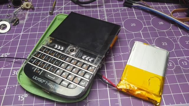 A partially assembled lilygo t deck with half a 3d printed case and a LiPo connected, on a messy desk. 