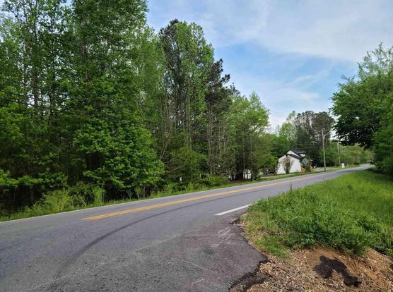 Rural road with trees, grassy areas, and a small house visible along the roadside.
