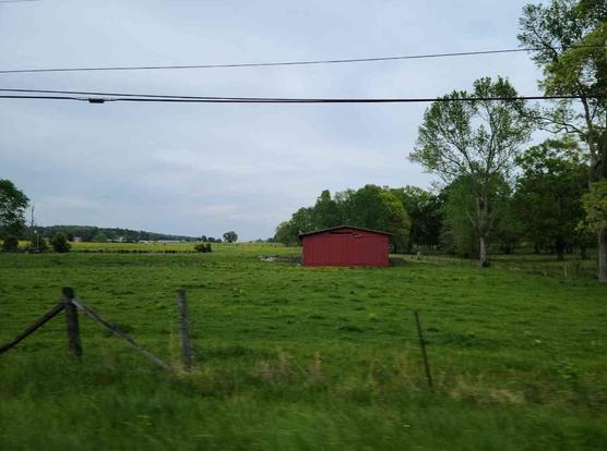 Rural landscape with a red barn in a grassy field, bordered by trees and power lines.