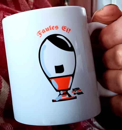 Kaffeetasse mit einem Eierbecher als Aufdruck. Das Ei in diesem Eierbecher sieht aus wie Adolf. Dazu die Überschrift: Faules Ei.