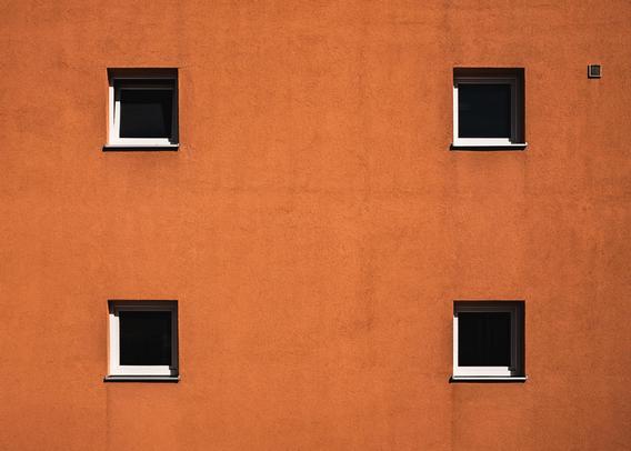Minimalist photo of an orange stucco building facade with four evenly spaced square windows, two on the top row and two on the bottom. The clean grid layout and bold wall color create a striking geometric composition.

