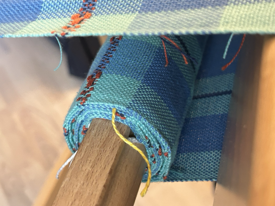 Close up look at handwoven blue checked fabric wrapping around the cloth beam of a hand loom 